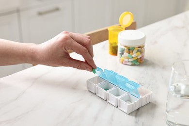 Woman with pills, organizer and glass of water at white marble table, closeup