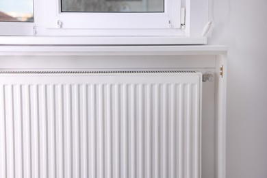 Photo of Modern radiator on wall under window indoors. Central heating system