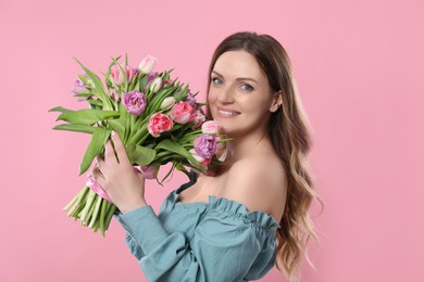 Happy young woman with bouquet of beautiful tulips on pink background