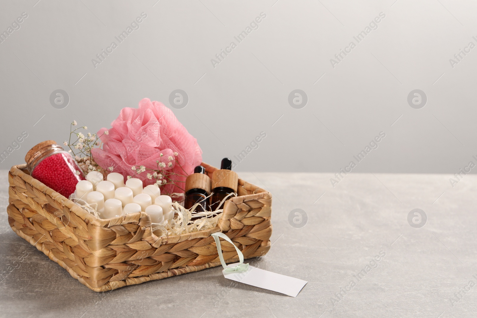 Photo of Spa gift set of different luxury products in wicker basket on grey table, space for text