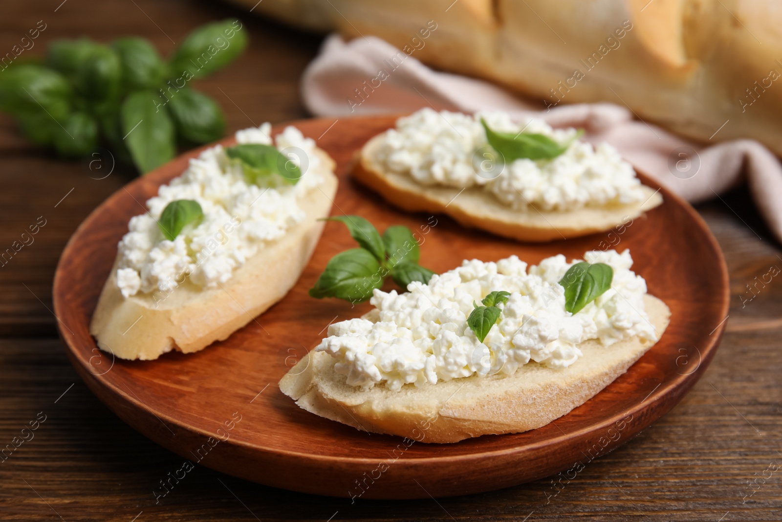 Photo of Bread with cottage cheese and basil on wooden table, closeup