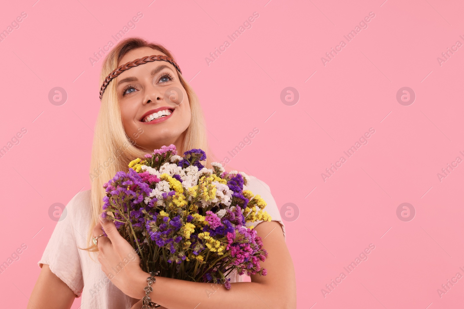 Photo of Portrait of smiling hippie woman with bouquet of flowers on pink background. Space for text
