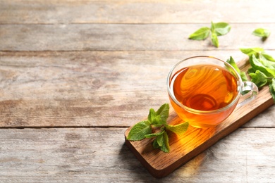 Photo of Cup with hot aromatic mint tea and fresh leaves on wooden board