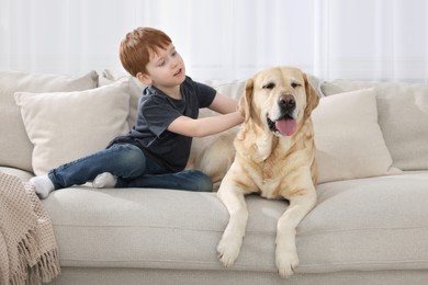 Photo of Cute child with his Labrador Retriever on sofa at home. Adorable pet