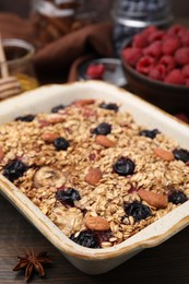 Photo of Tasty baked oatmeal with berries and almonds in baking tray on wooden table, closeup
