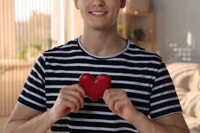 Photo of Happy volunteer holding red heart with hands indoors, closeup