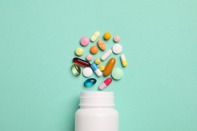 Plastic medical bottle with many different pills on turquoise background, flat lay