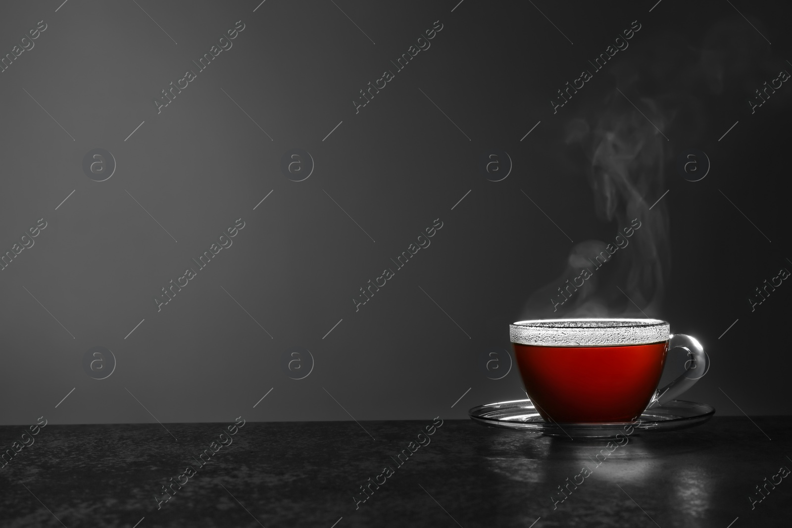 Photo of Glass cup of hot tea on stone table against grey background, space for text