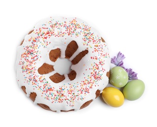 Glazed Easter cake with sprinkles, painted eggs and flowers on white background, top view