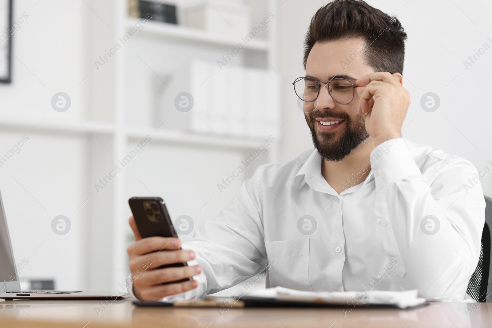 Photo of Handsome young man using smartphone at table in office