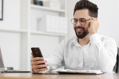 Photo of Handsome young man using smartphone at table in office