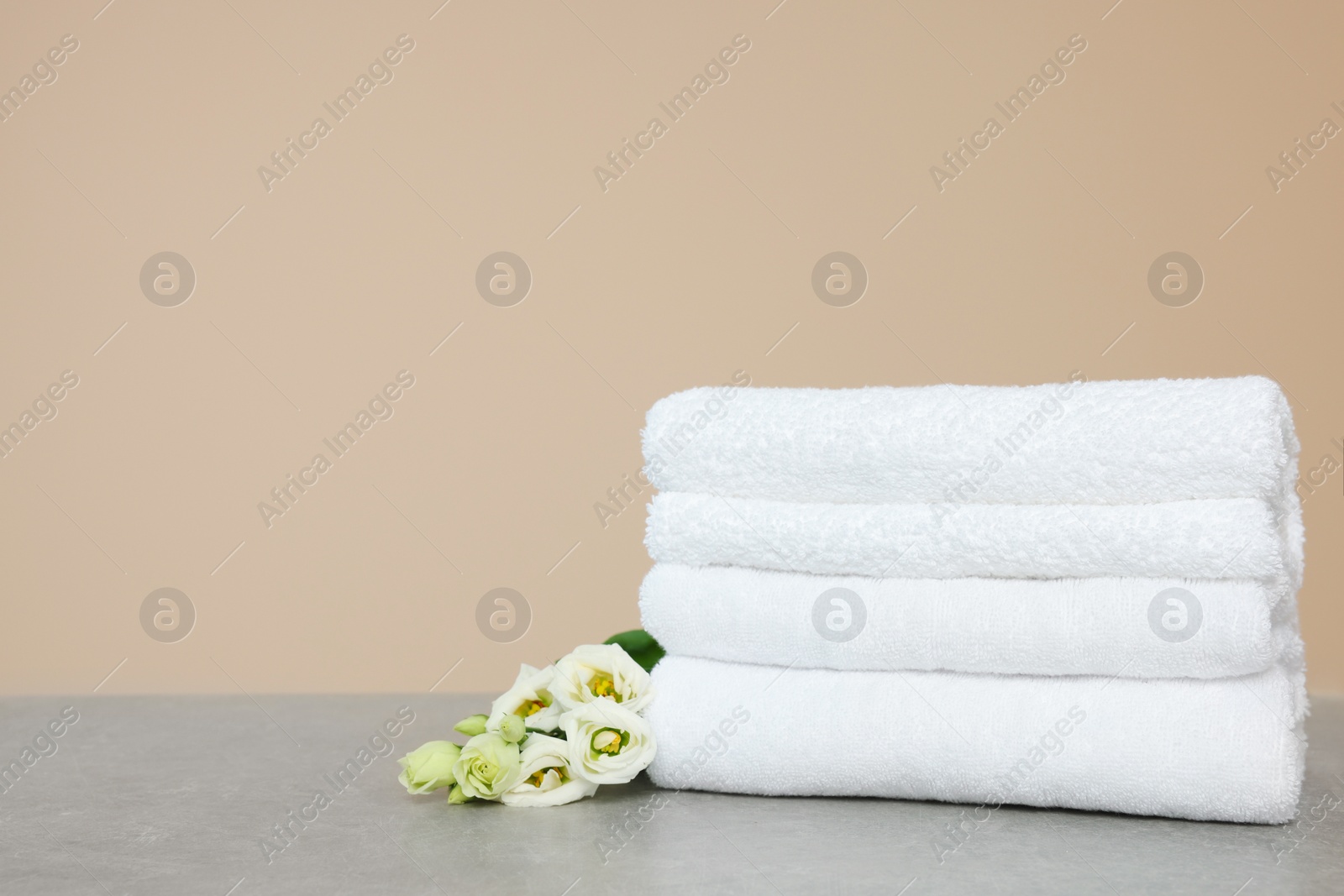 Photo of Soft folded towels and eustoma flowers on grey table, space for text