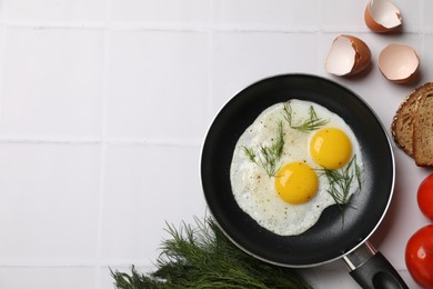 Photo of Frying pan with tasty cooked eggs, dill and other products on white tiled table, flat lay. Space for text