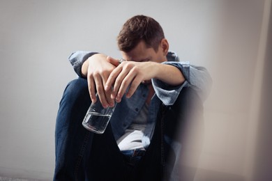 Addicted man with alcoholic drink near beige wall