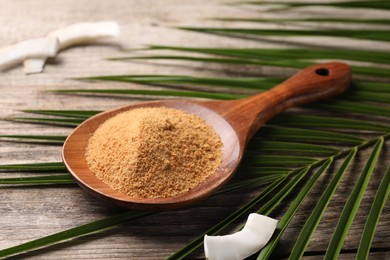 Photo of Spoon with coconut sugar, slice of fruit and palm leaves on wooden table, closeup