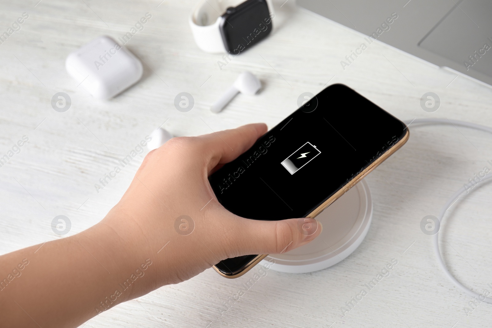 Photo of Woman putting mobile phone onto wireless charger at white wooden table, closeup