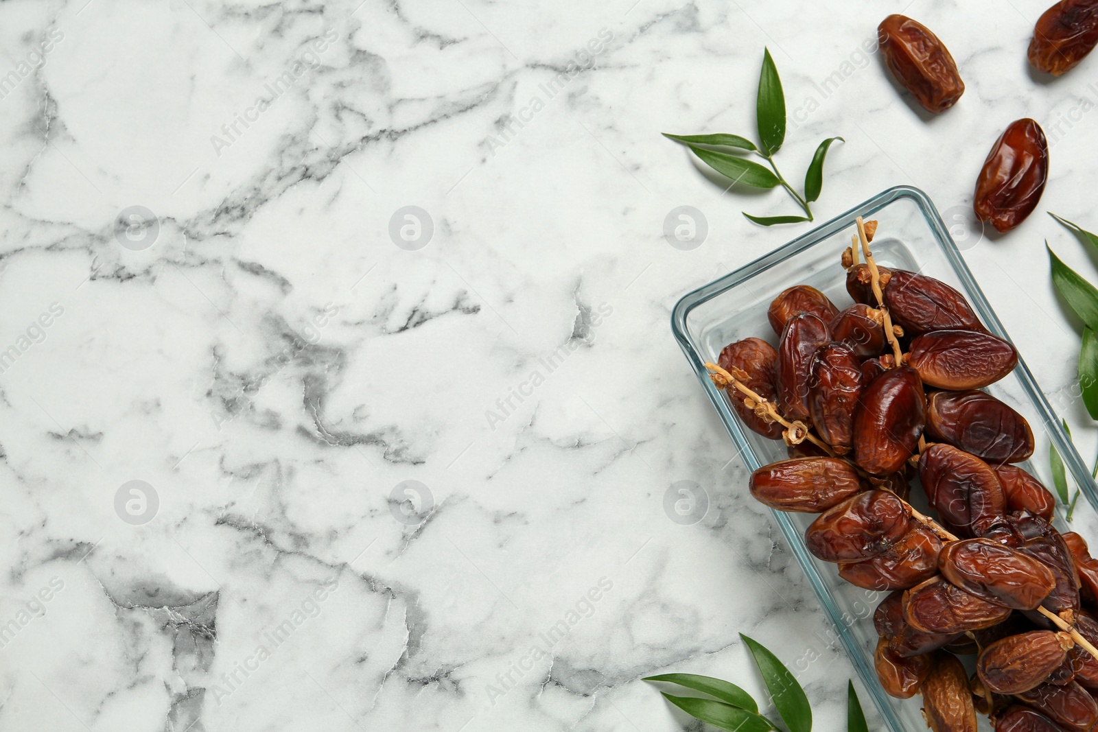 Photo of Tasty sweet dried dates and green leaves on white marble table, flat lay. Space for text