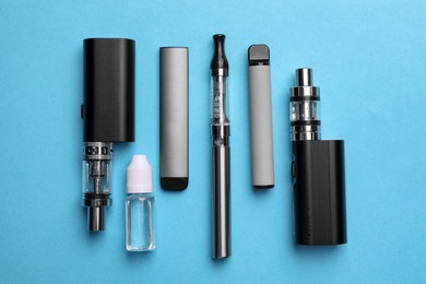 Photo of Different electronic cigarettes and liquid solution on light blue background, flat lay
