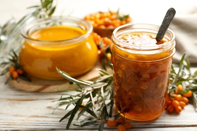 Photo of Delicious sea buckthorn jam and fresh berries on white wooden table. Space for text