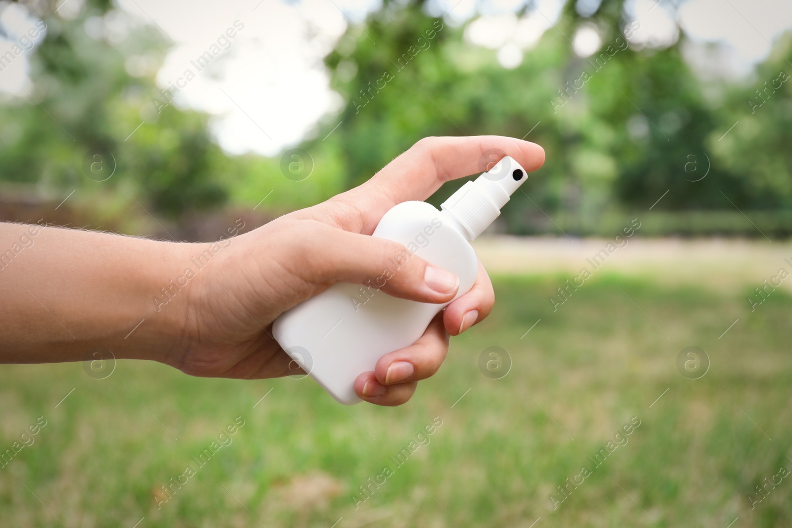 Photo of Woman with bottle of insect repellent spray outdoors, closeup