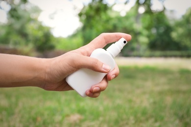 Photo of Woman with bottle of insect repellent spray outdoors, closeup