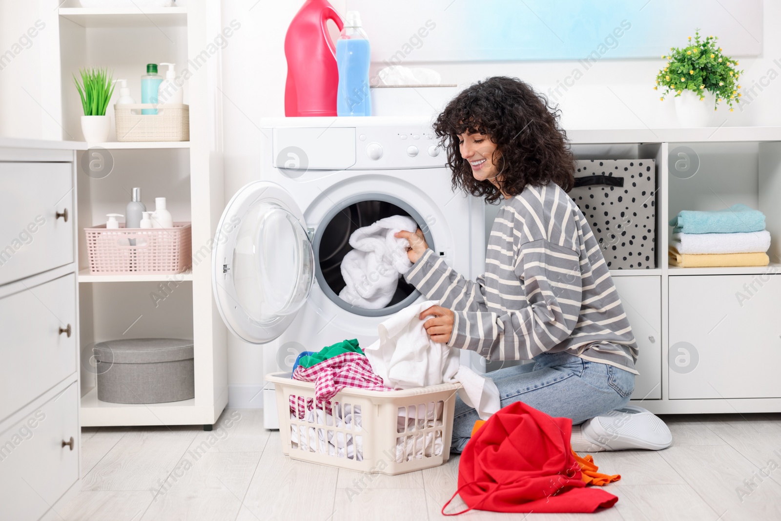 Photo of Happy woman putting laundry into washing machine indoors