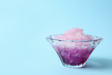 Photo of Shaving ice in glass dessert bowl on light blue background, closeup. Space for text