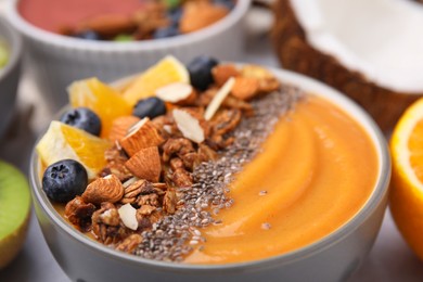 Photo of Bowl of delicious fruit smoothie with fresh orange slices, blueberries and granola on table, closeup
