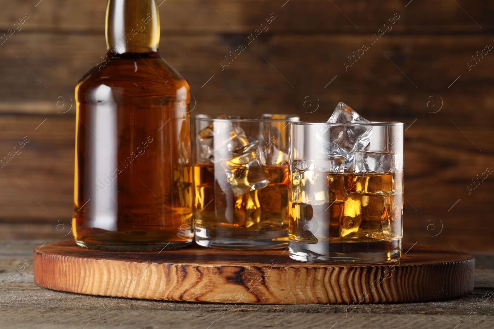 Photo of Whiskey with ice cubes in glasses and bottle on wooden table, closeup