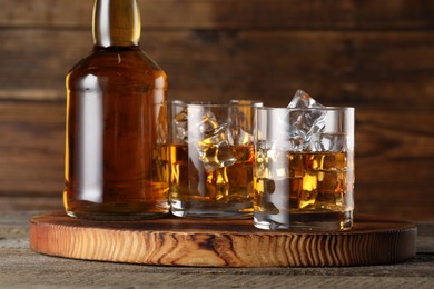 Whiskey with ice cubes in glasses and bottle on wooden table, closeup