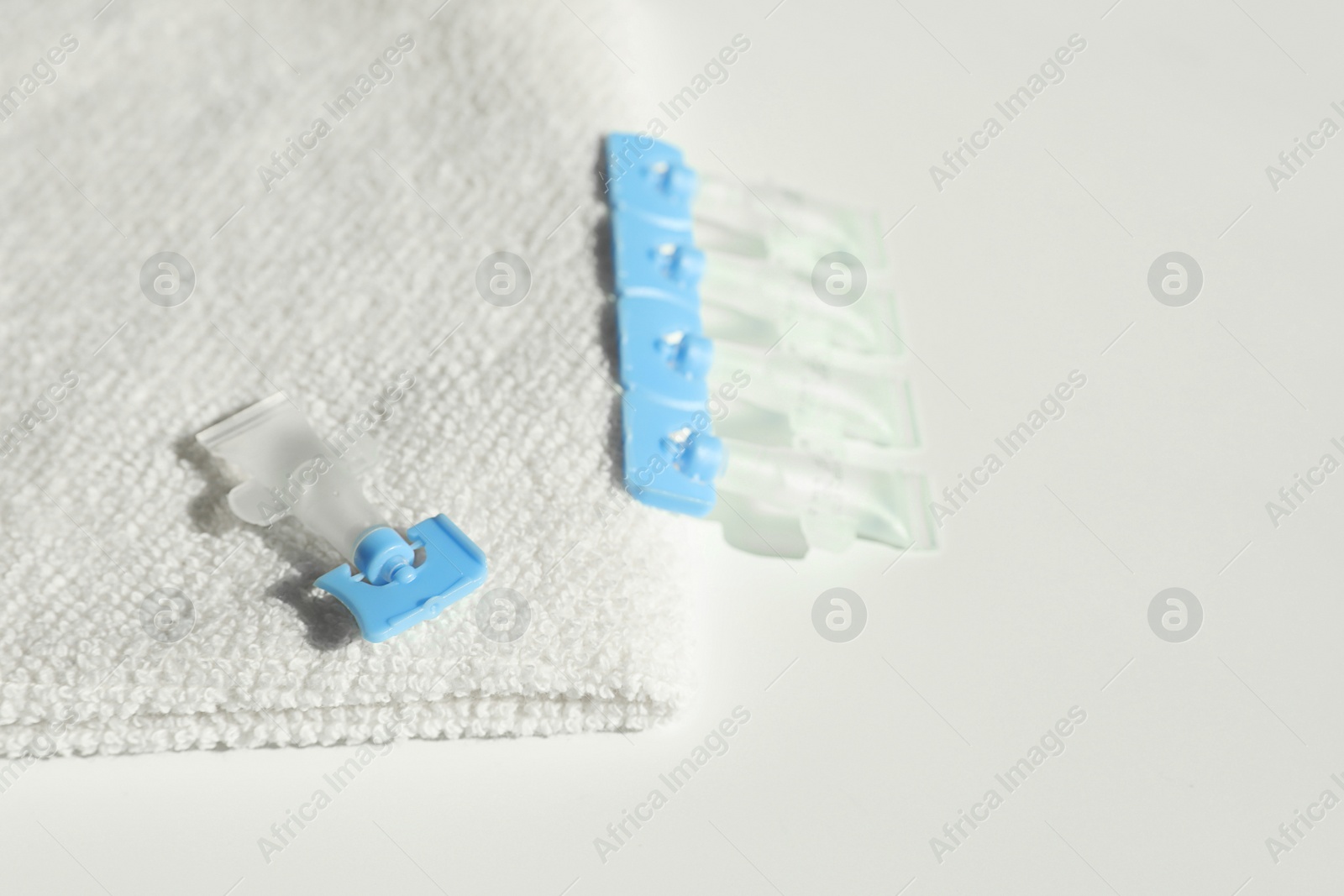 Photo of Single dose eye drops and towel on white table, closeup