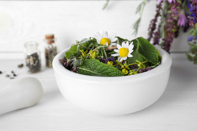 Photo of Mortar with healing herbs and pestle on white wooden table, closeup