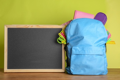 Photo of Small chalkboard and backpack with different school stationery on table