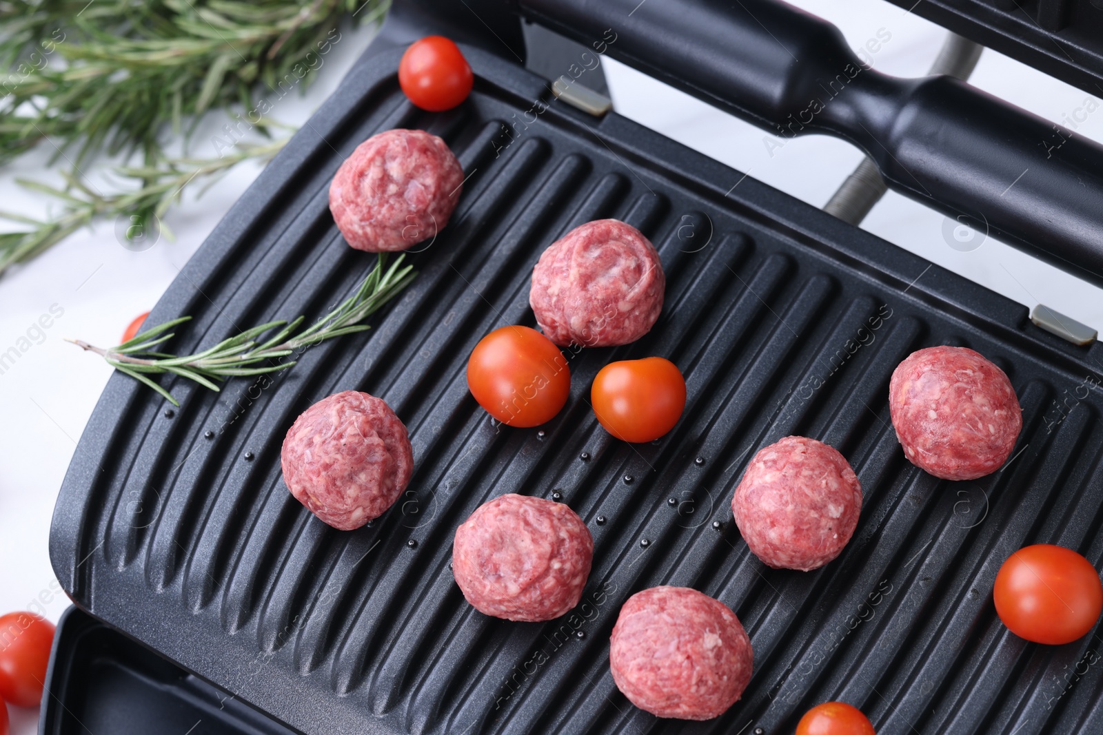 Photo of Electric grill with meatballs, tomatoes and rosemary on white table, above view