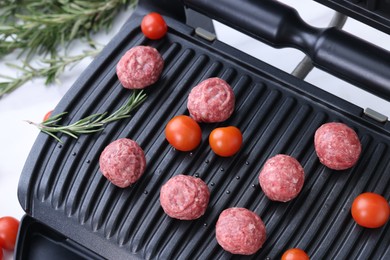 Electric grill with meatballs, tomatoes and rosemary on white table, above view