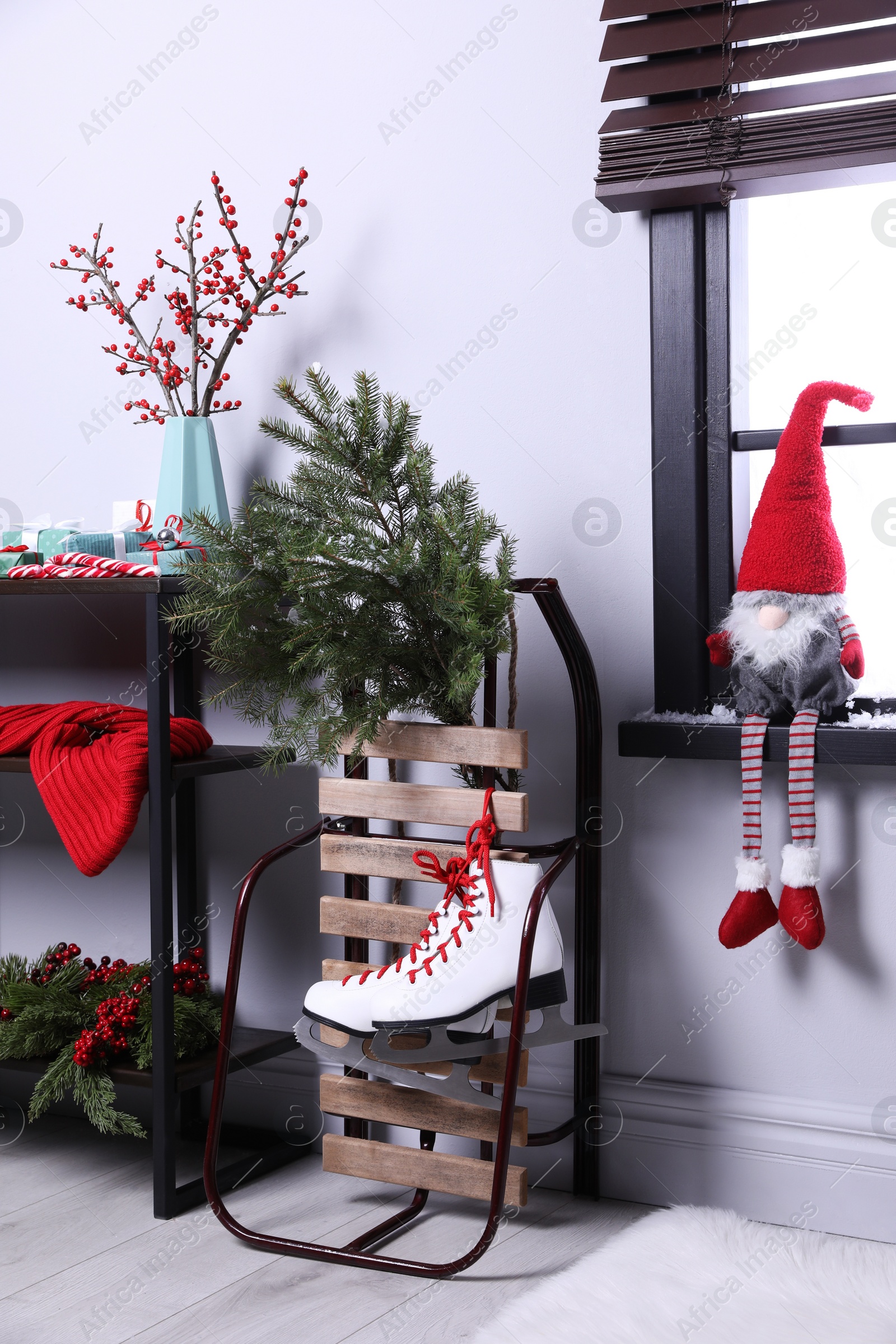 Photo of Sleigh with pair of ice skates and fir branches near window in decorated room