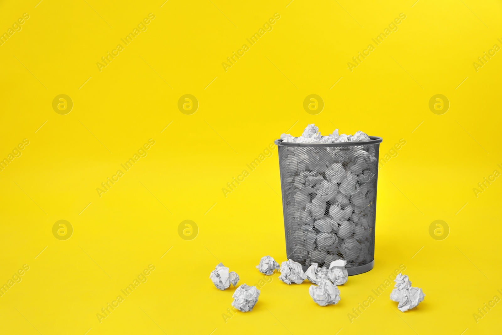 Photo of Metal bin with crumpled paper on color background, space for text