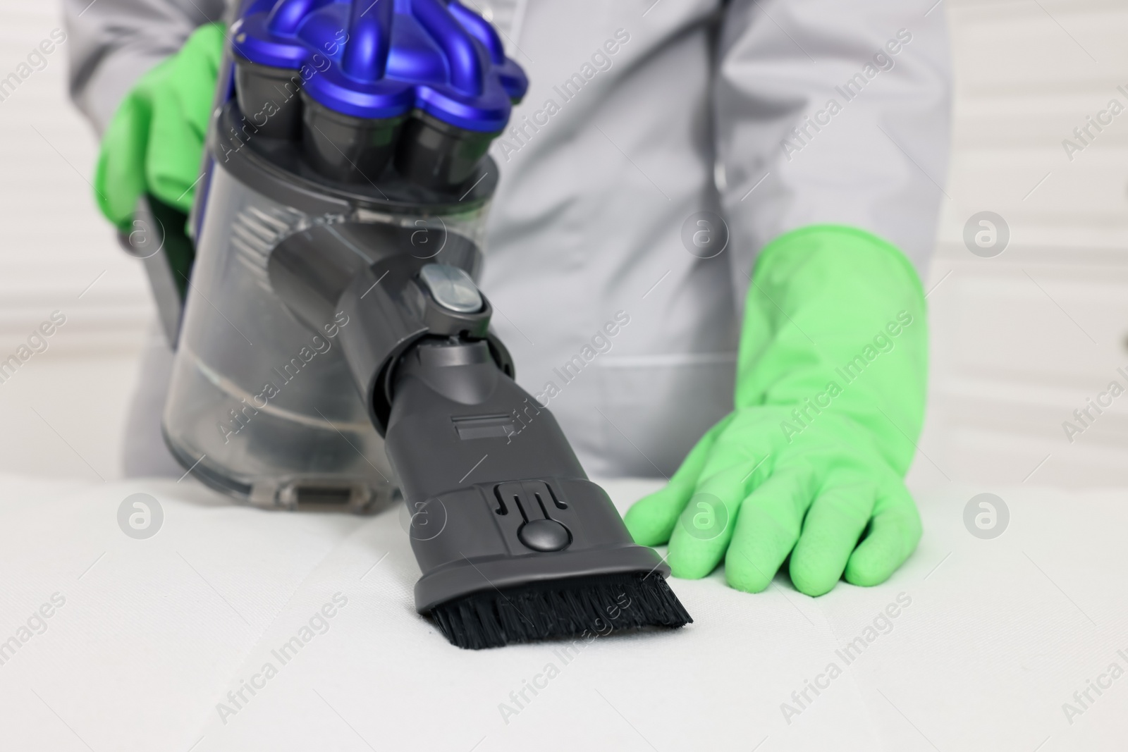 Photo of Woman in gloves disinfecting mattress with vacuum cleaner indoors, closeup