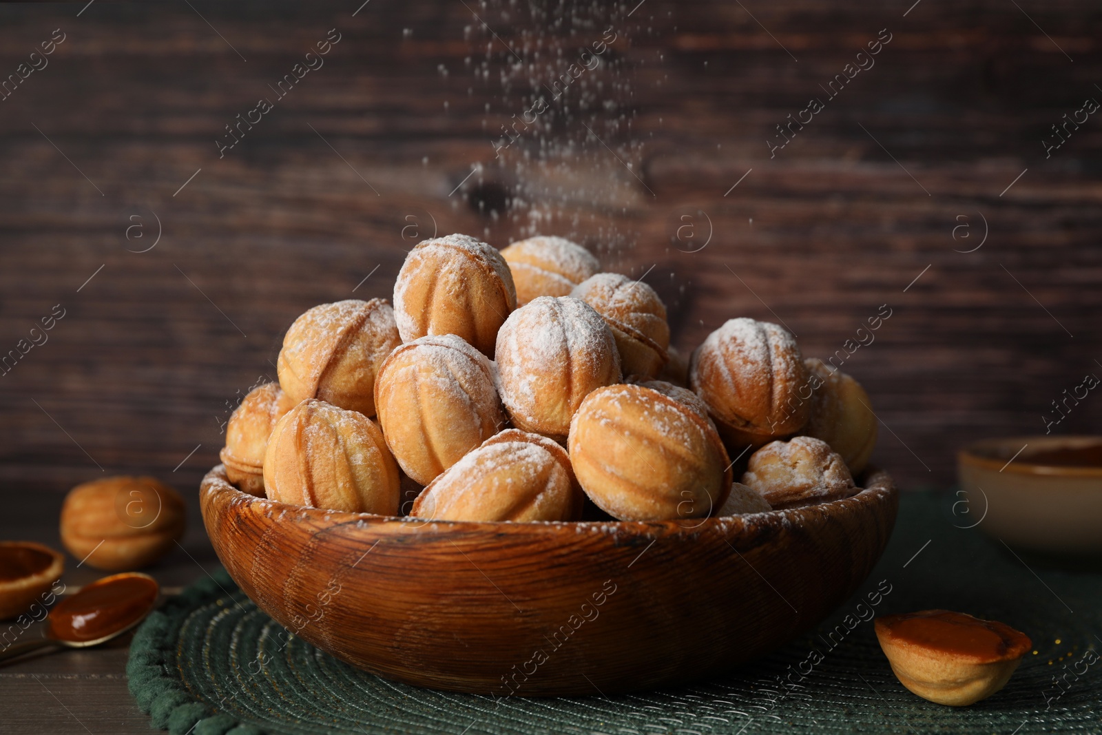 Photo of Bowl of delicious nut shaped cookies with boiled condensed milk on wooden table