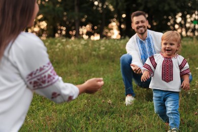 Photo of Happy parents in embroidered Ukrainian shirts playing with their cute daughter outdoors