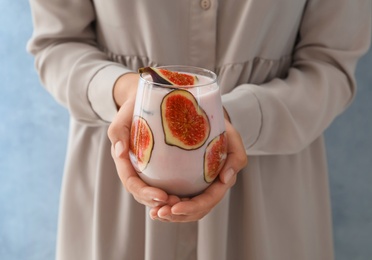 Photo of Woman holding fig smoothie on light blue background, closeup