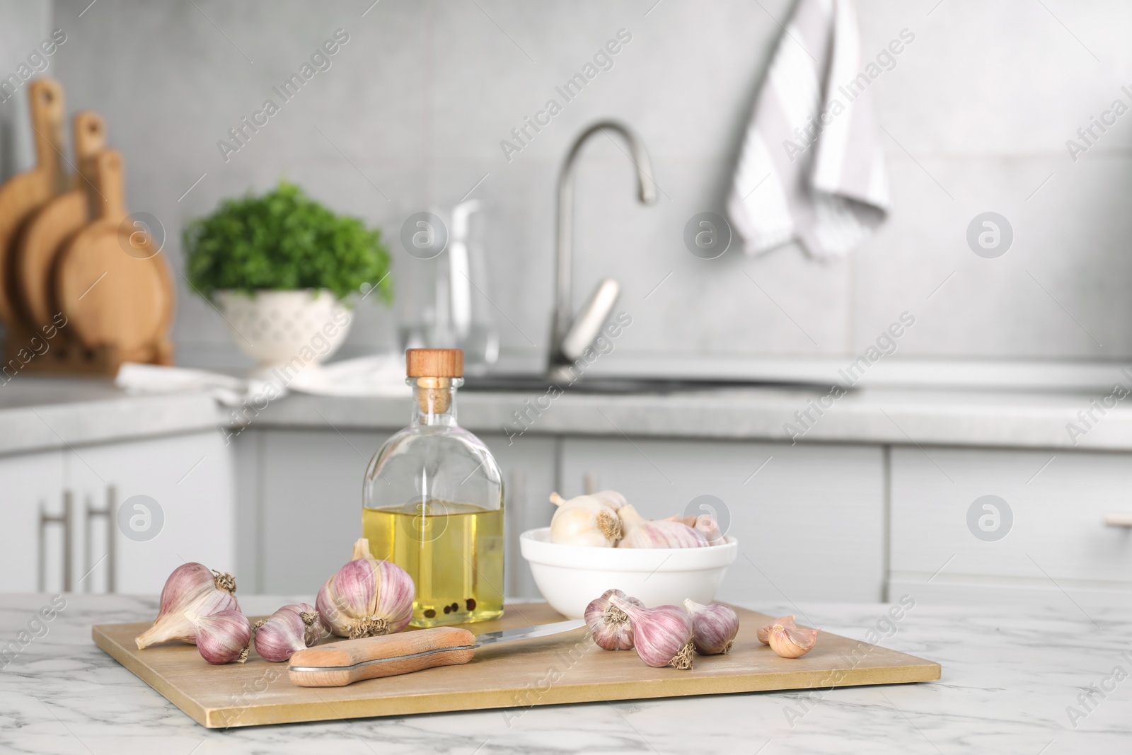 Photo of Fresh raw garlic, knife and oil on white marble table, space for text