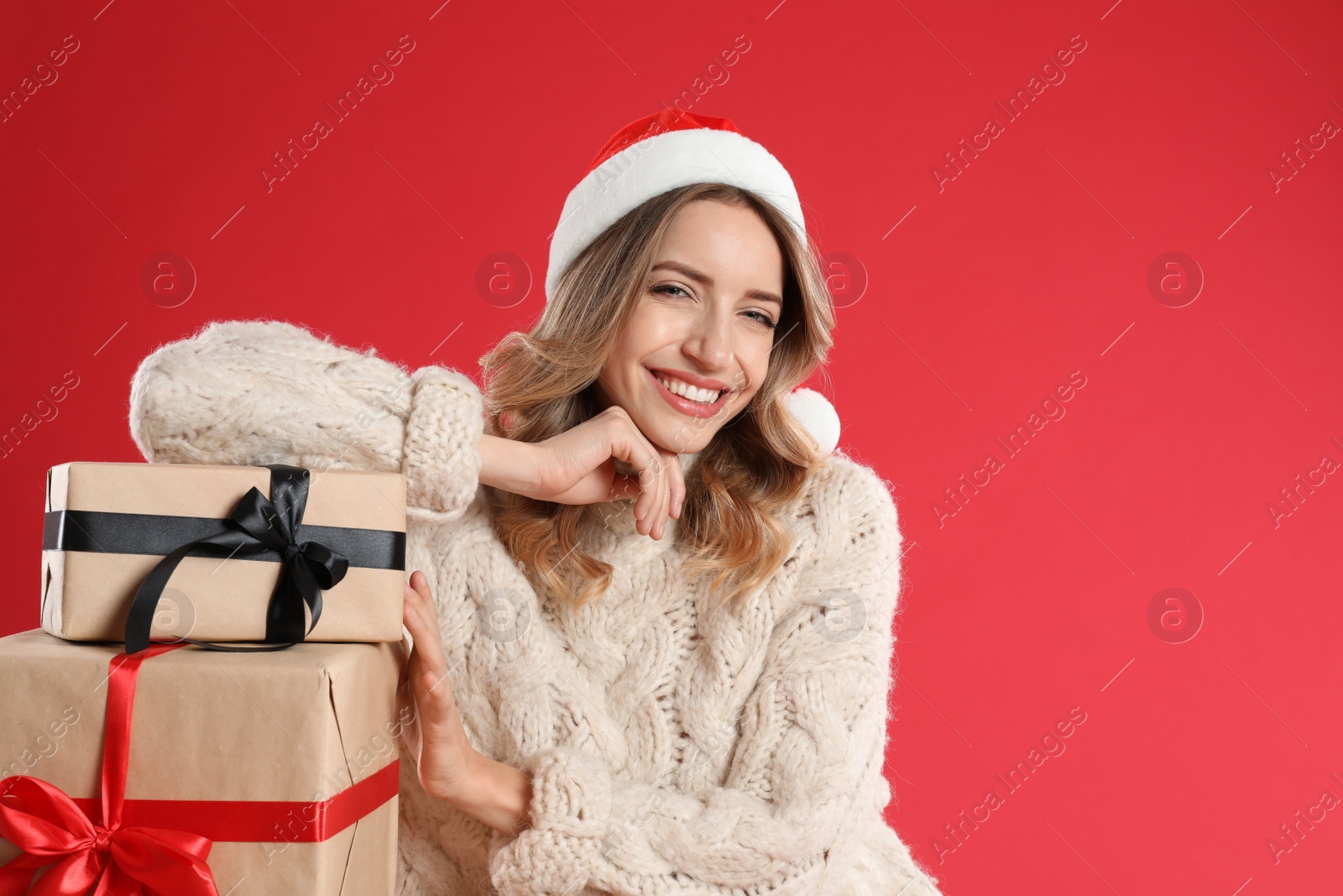 Photo of Beautiful young woman in Santa hat with Christmas presents on red background