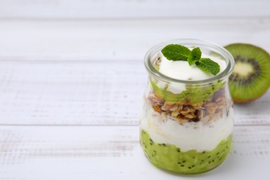 Photo of Delicious dessert with kiwi, yogurt and muesli on white wooden table, space for text