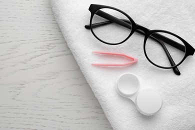 Photo of Case with contact lenses, tweezers, glasses and towel on white wooden table, top view. Space for text
