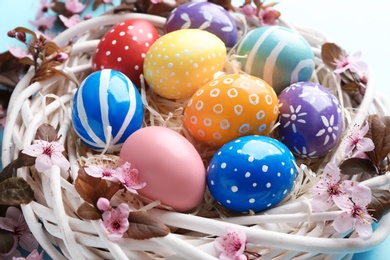 Photo of Painted Easter eggs in nest with flowers on color background, closeup