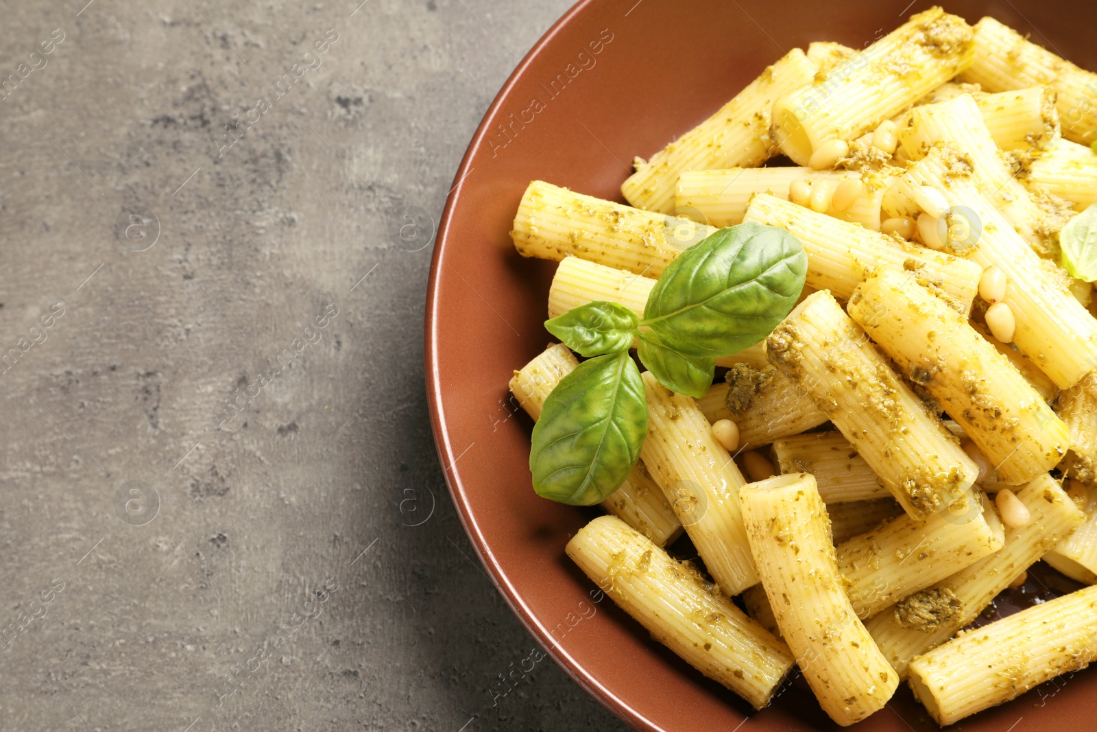 Photo of Plate of delicious basil pesto pasta on grey background, top view with space for text