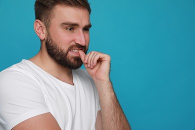 Man biting his nails on light blue background, space for text. Bad habit