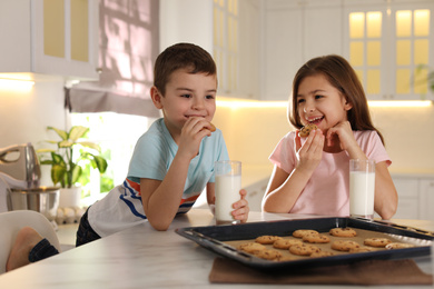Photo of Cute little children eating cookies with milk in kitchen. Cooking pastry