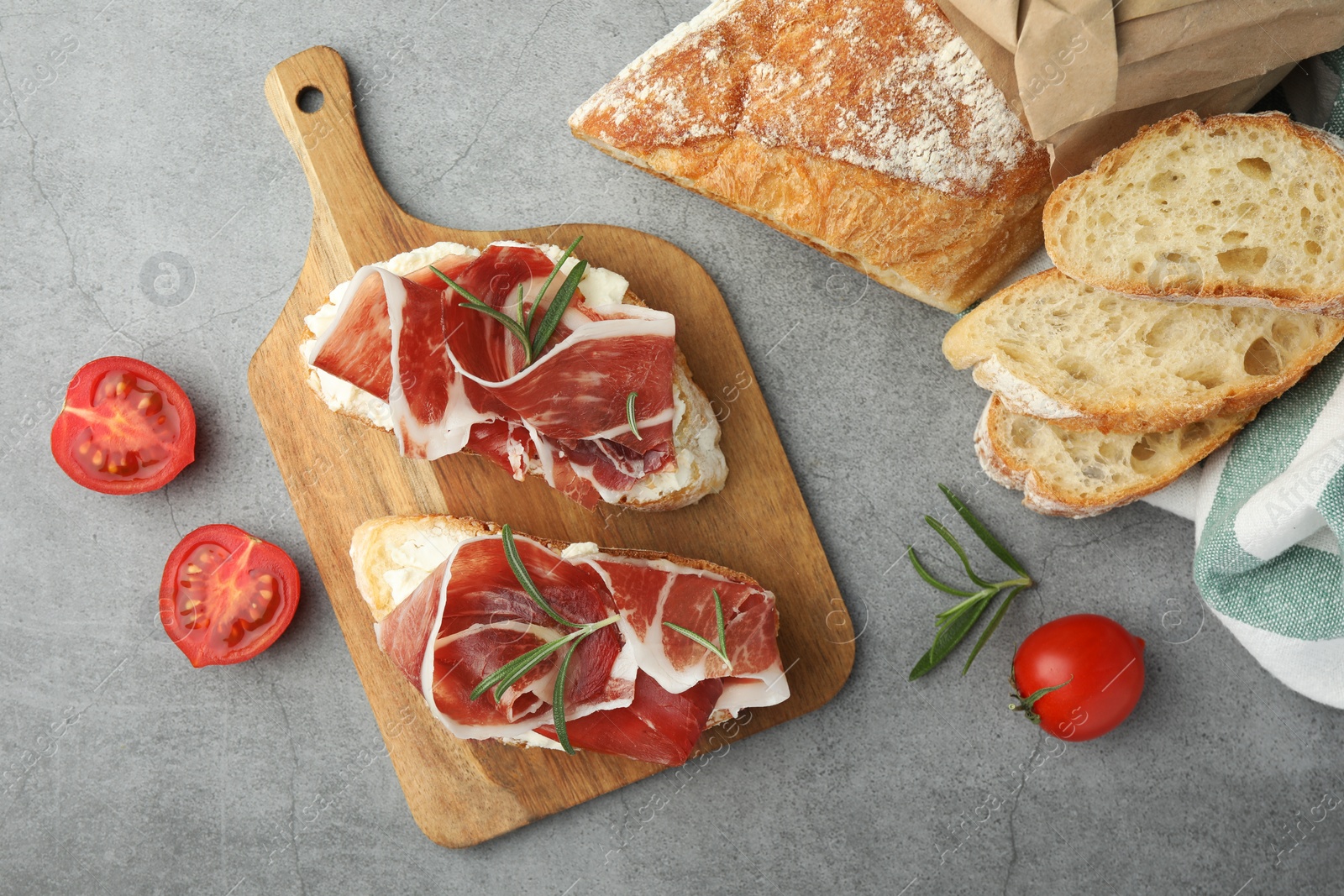 Photo of Tasty sandwiches with cured ham, rosemary and tomatoes on grey table, flat lay